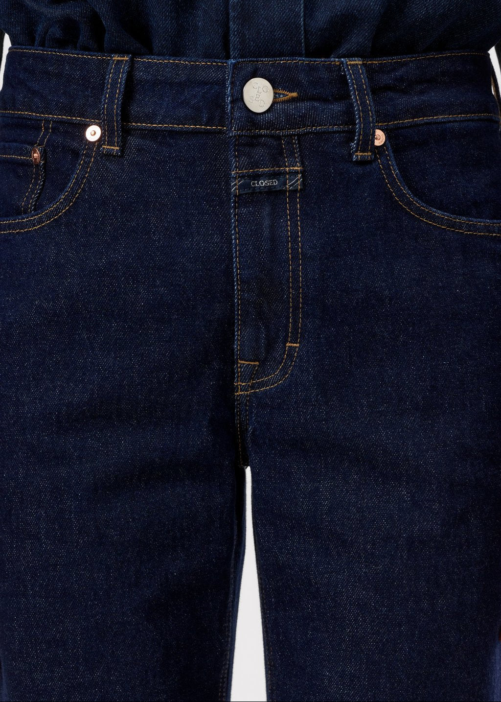 Close-up of dark indigo blue denim jeans showing the front waistband, button closure, belt loops, and front pockets.