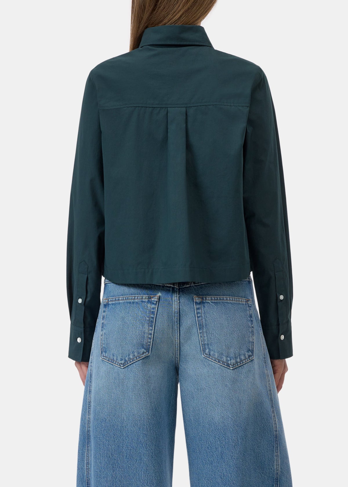 A model shown from the back wearing a dark teal-green cropped button-up shirt and light blue wide-leg jeans against a light gray studio background.
