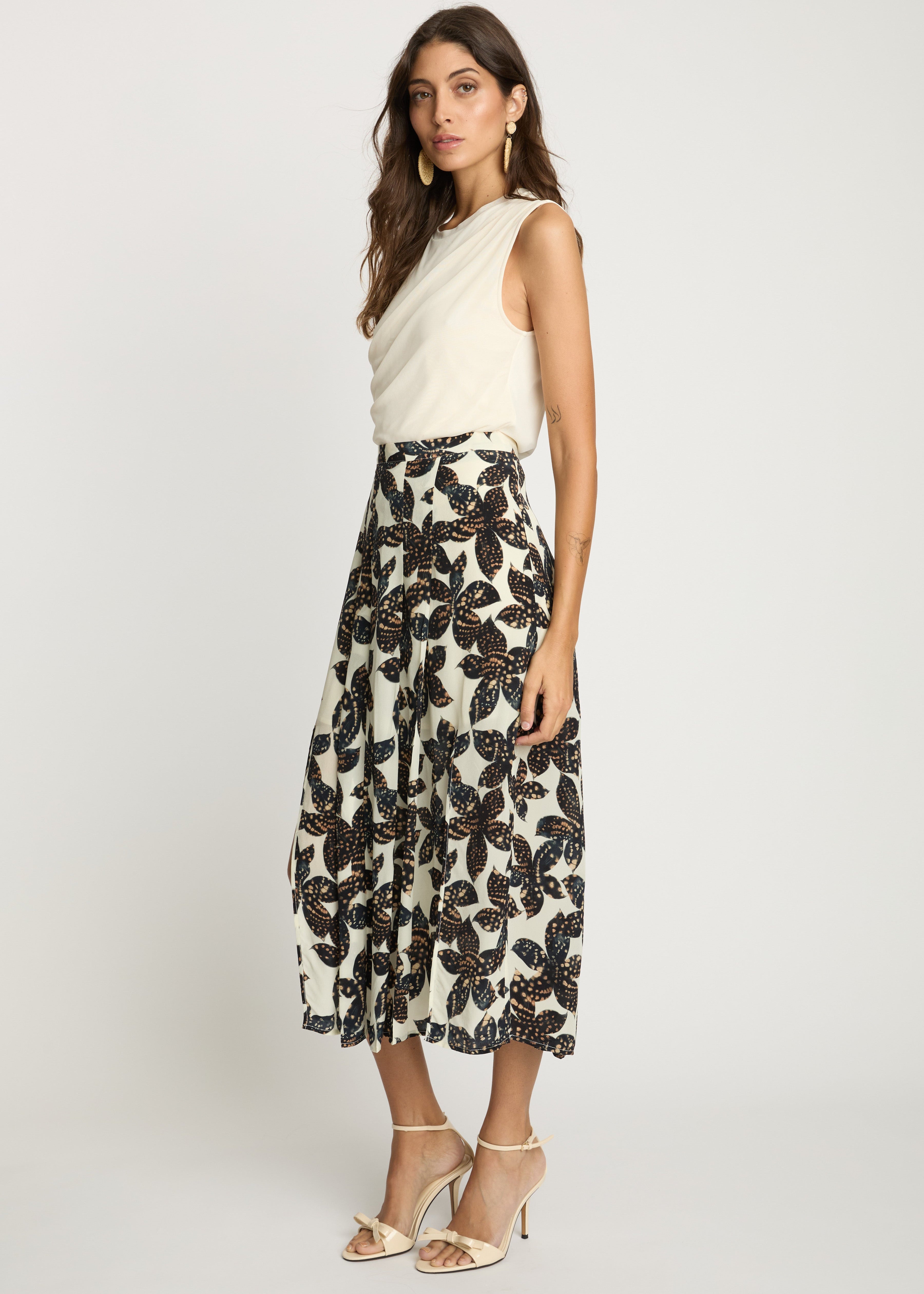Woman wearing a white sleeveless top and black floral skirt on a white background