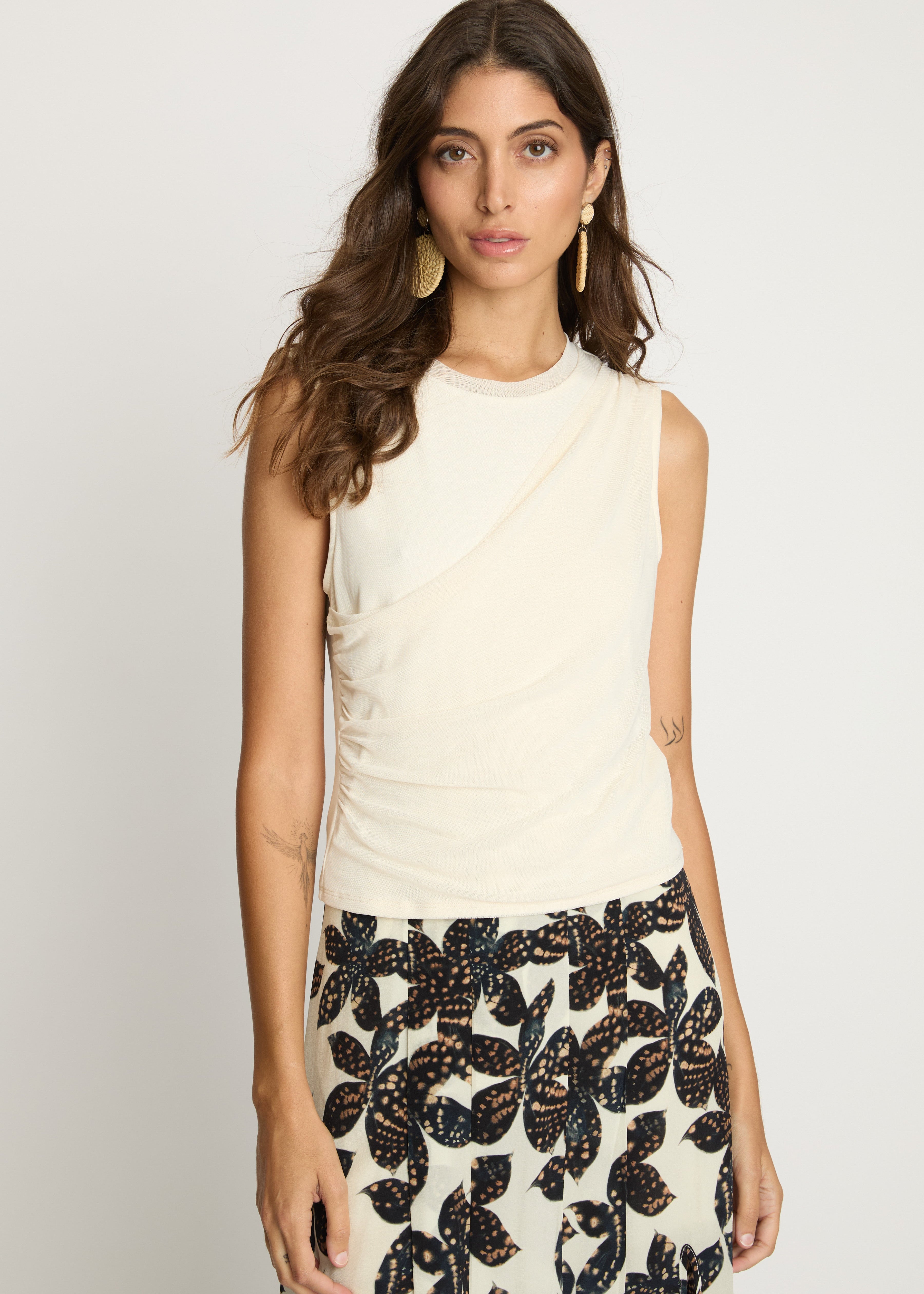 Woman wearing a sleeveless cream top and patterned skirt on a plain background