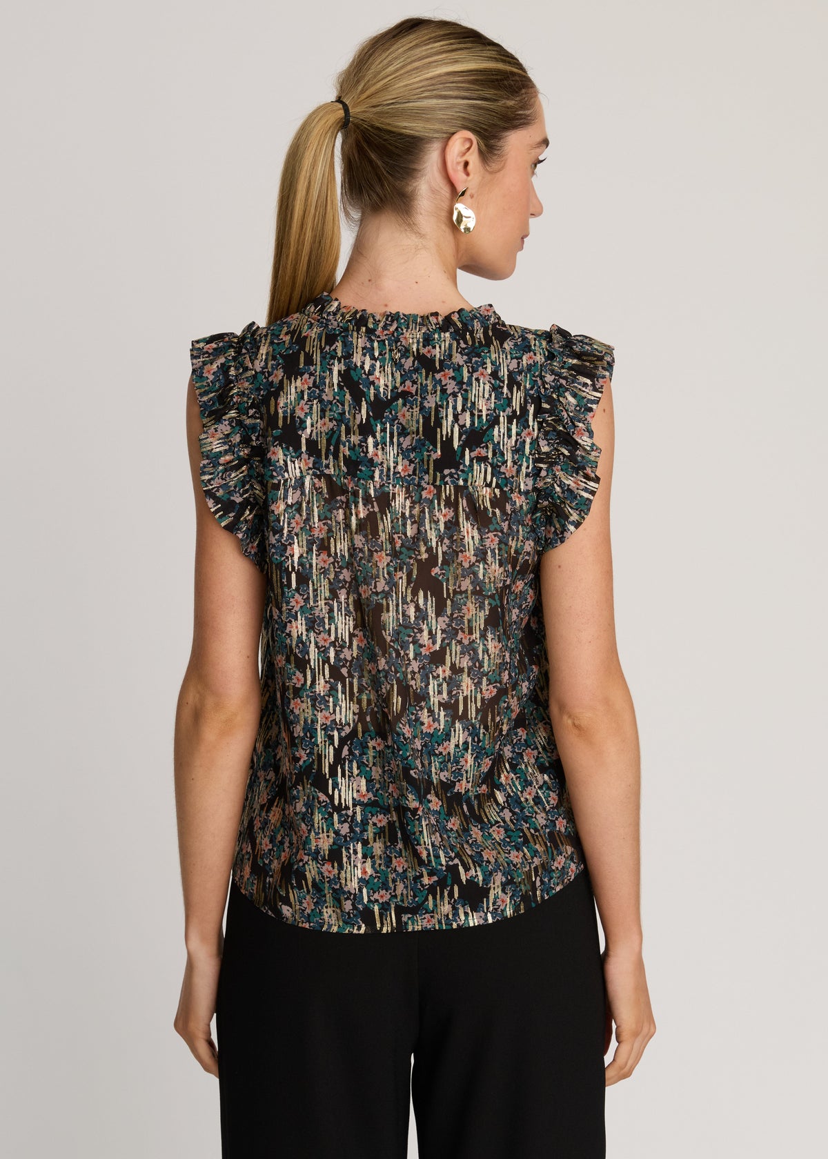 Woman wearing a patterned top with ruffled shoulders on a plain background