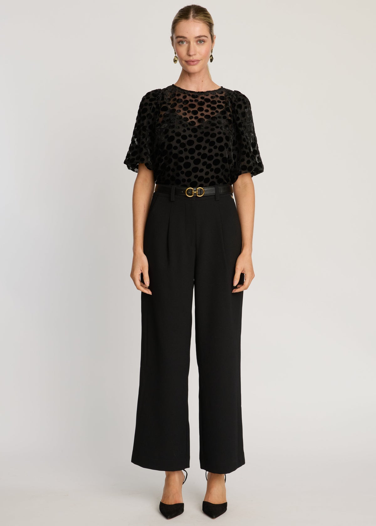 Woman wearing a black patterned top and black pants on a white background