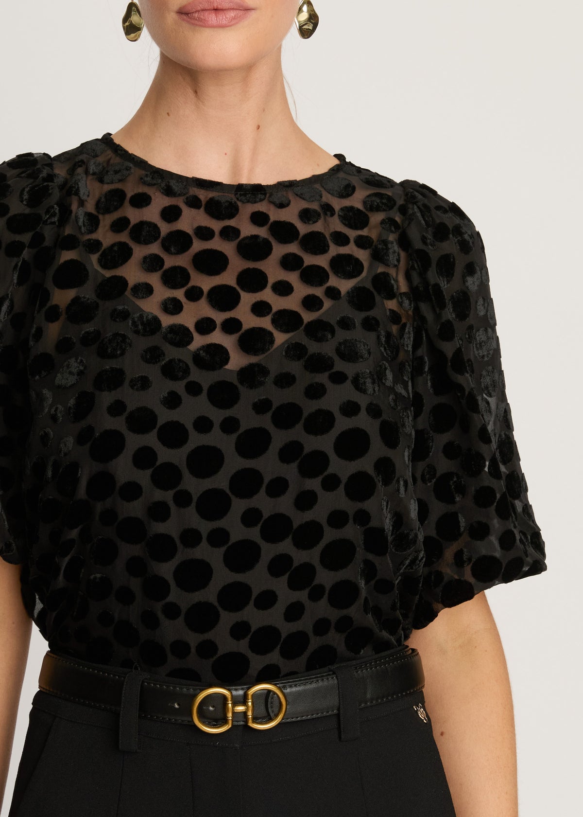 Black polka dot blouse worn by a model on a white background
