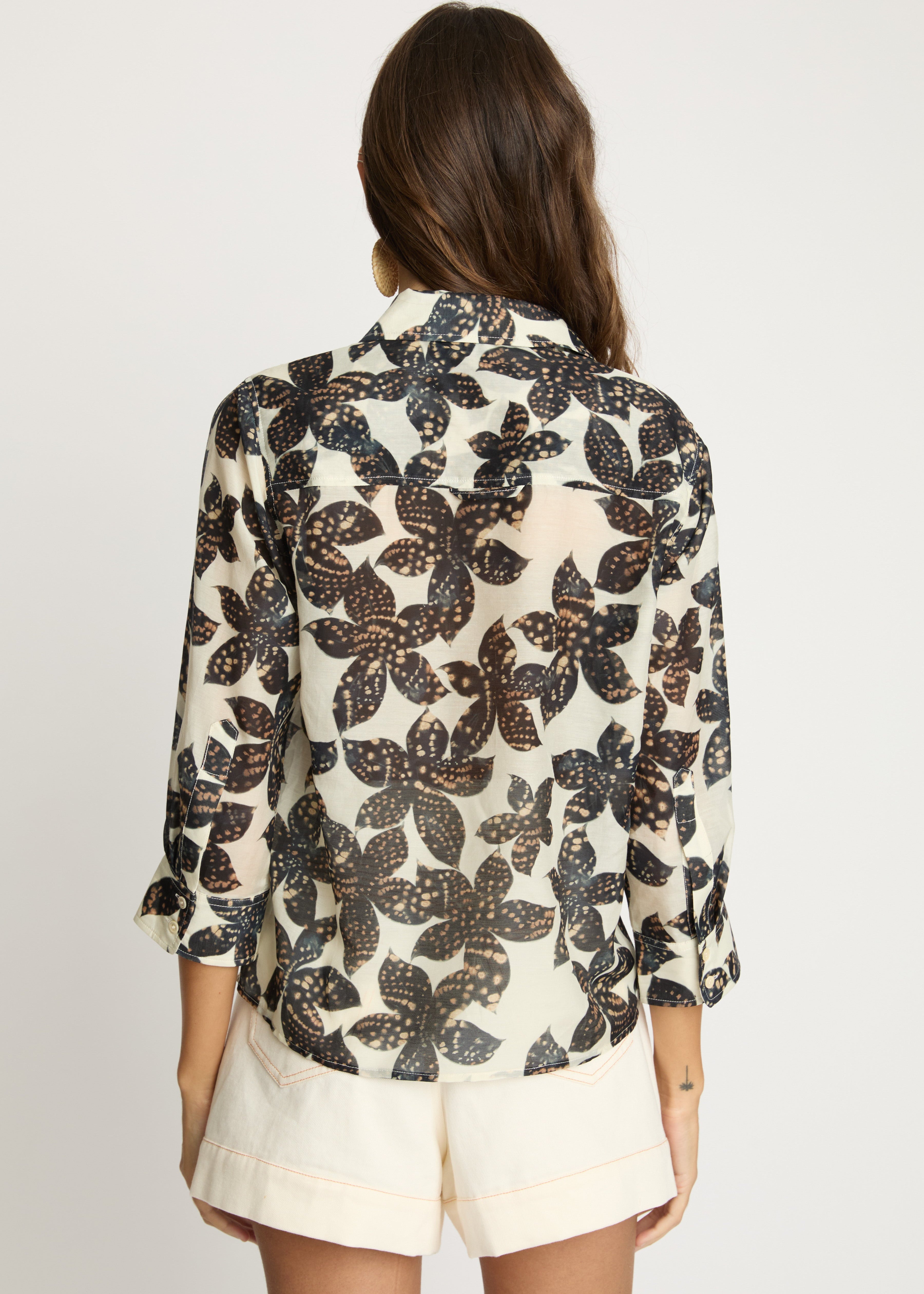 Woman wearing a floral blouse and shorts on a plain background