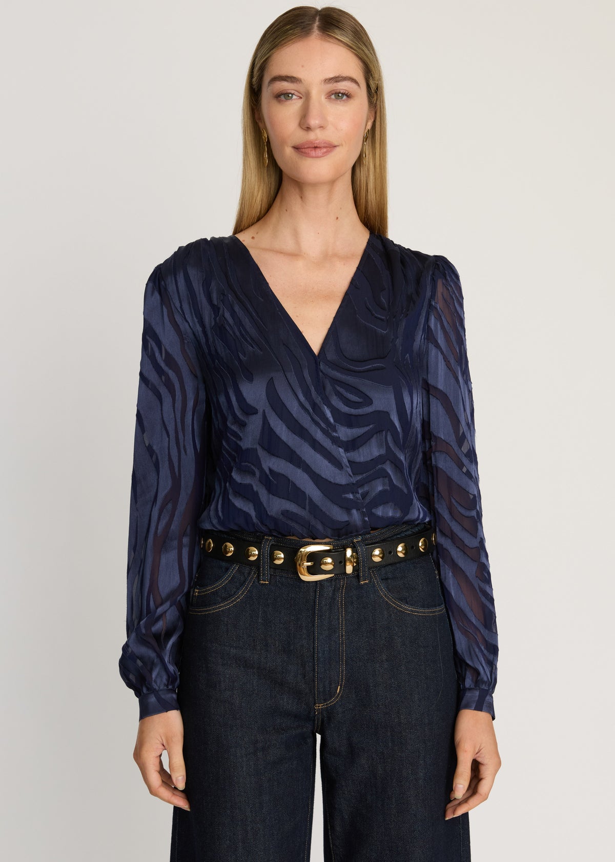 Woman wearing a navy patterned blouse and dark jeans on a white background