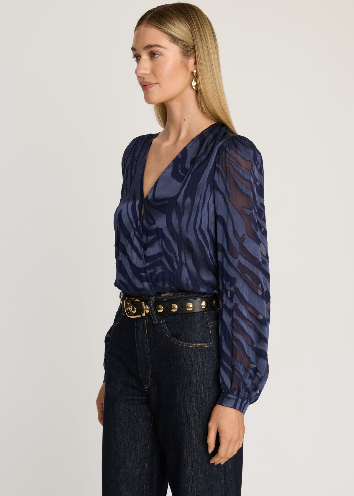 Woman wearing a dark blue patterned blouse and jeans on a plain background