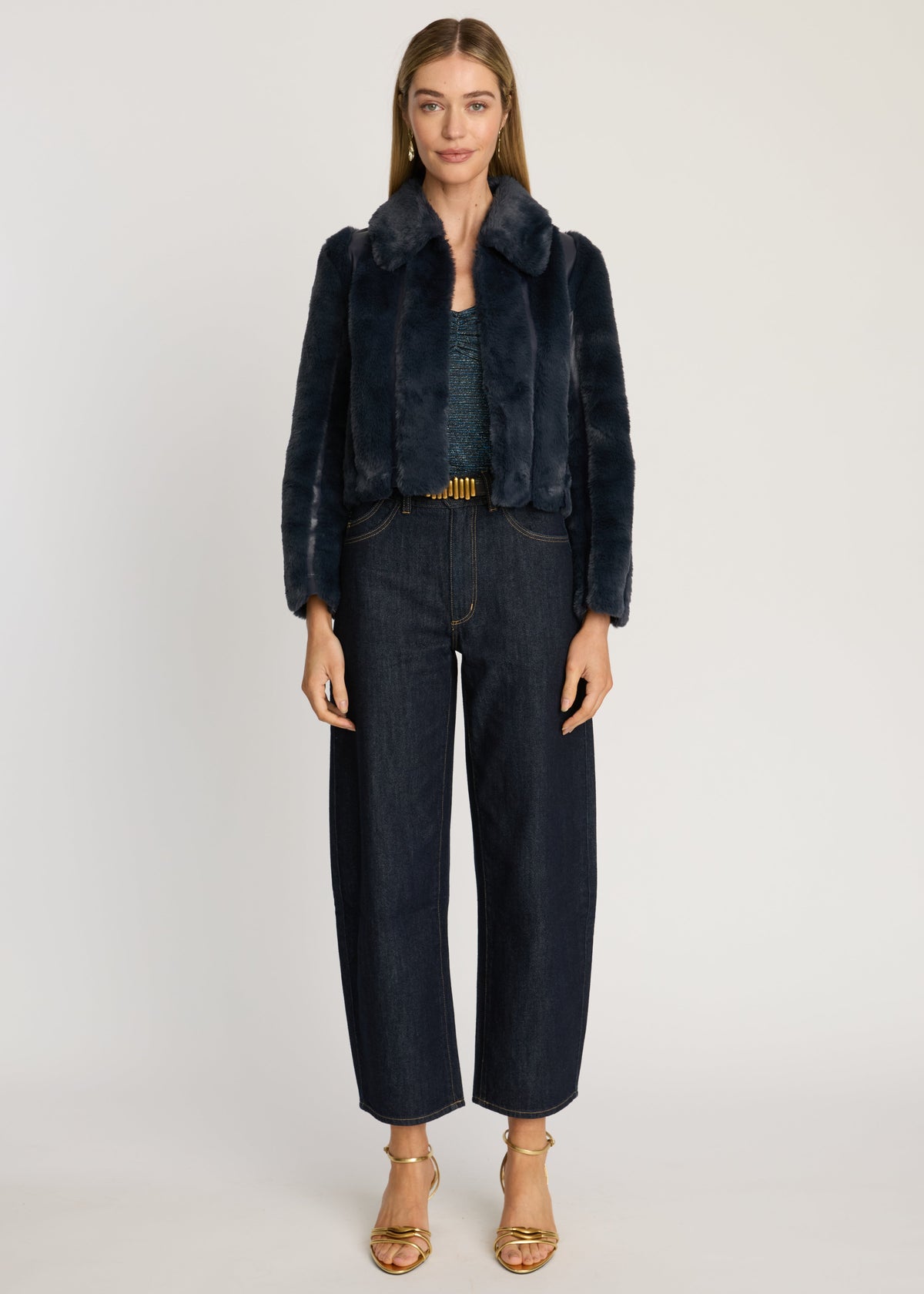 Woman wearing a dark blue fur-lined jacket and jeans on a white background