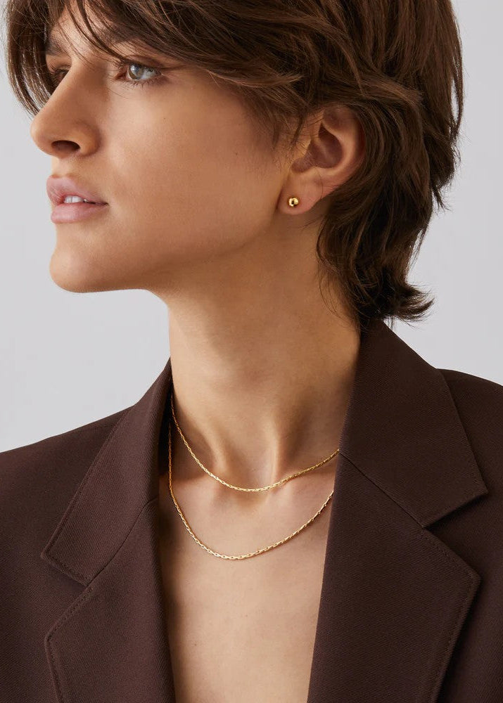 Woman wearing gold earrings and necklace against a neutral background