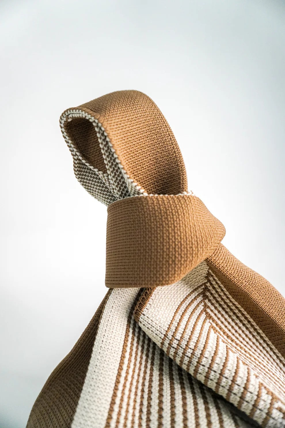 Close-up of a knitted brown and beige scarf on a light gray background