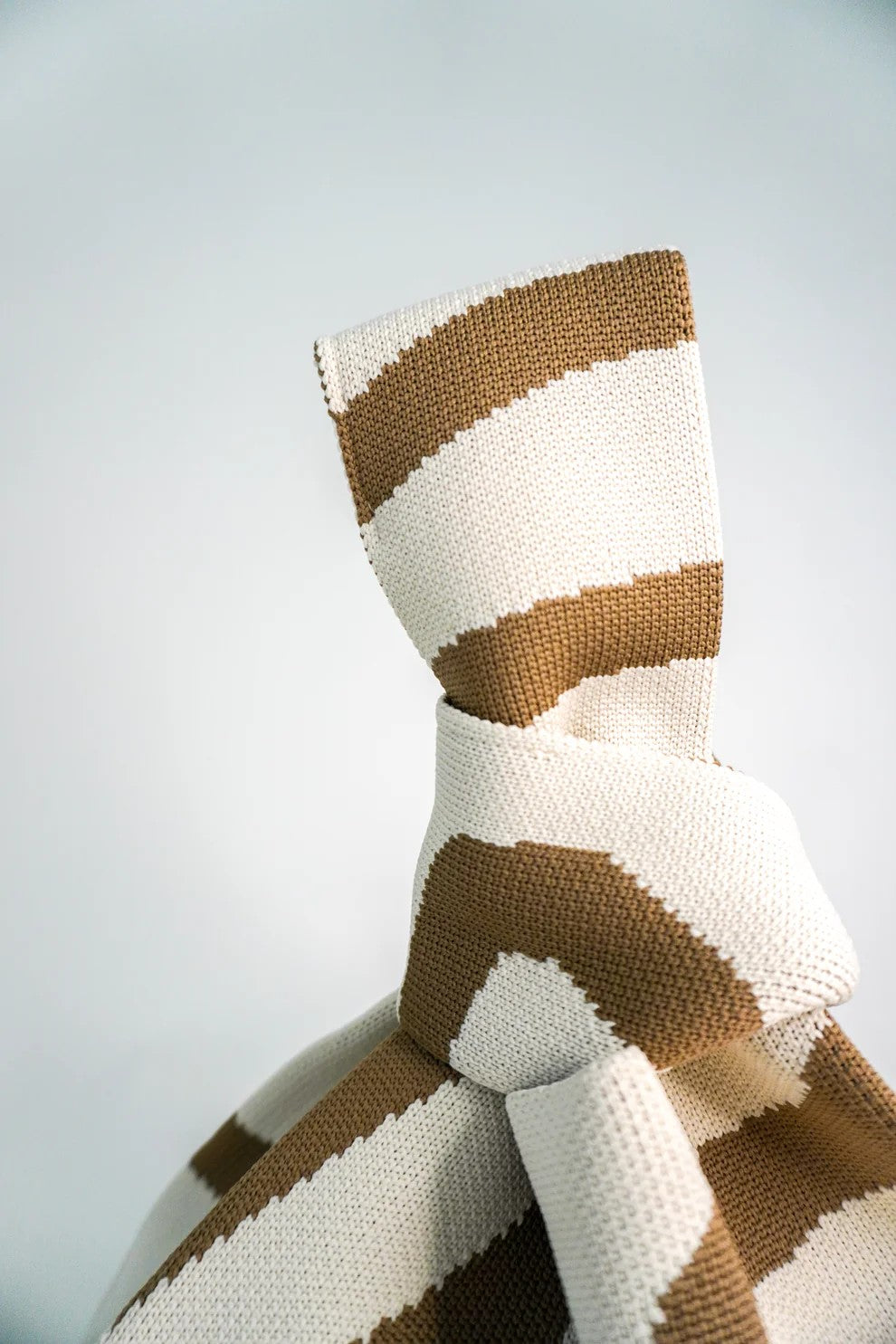 Knitted pillow with brown and white stripes on a light gray background
