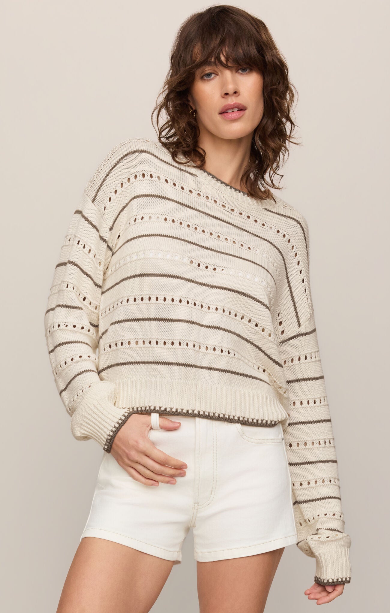 Woman wearing a patterned sweater and white shorts on a plain background