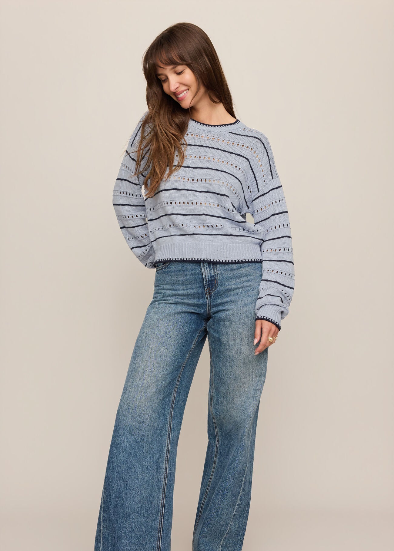 Woman wearing a striped sweater and blue jeans on a beige background