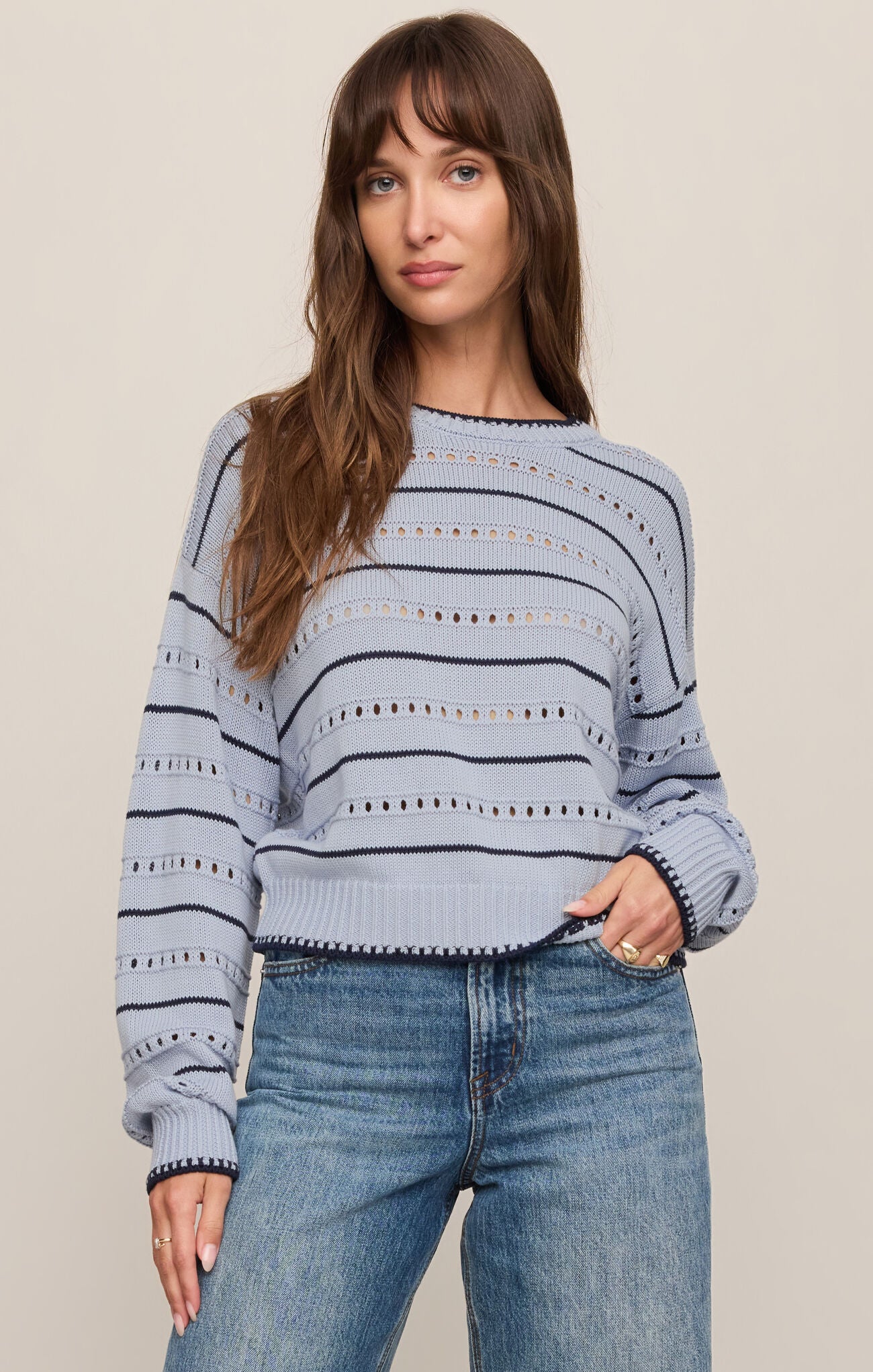 Woman wearing a blue striped sweater and jeans against a plain background