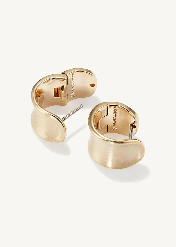 A pair of gold-toned curved hoop earrings with a brushed finish and post backs, displayed on a clean off-white background.