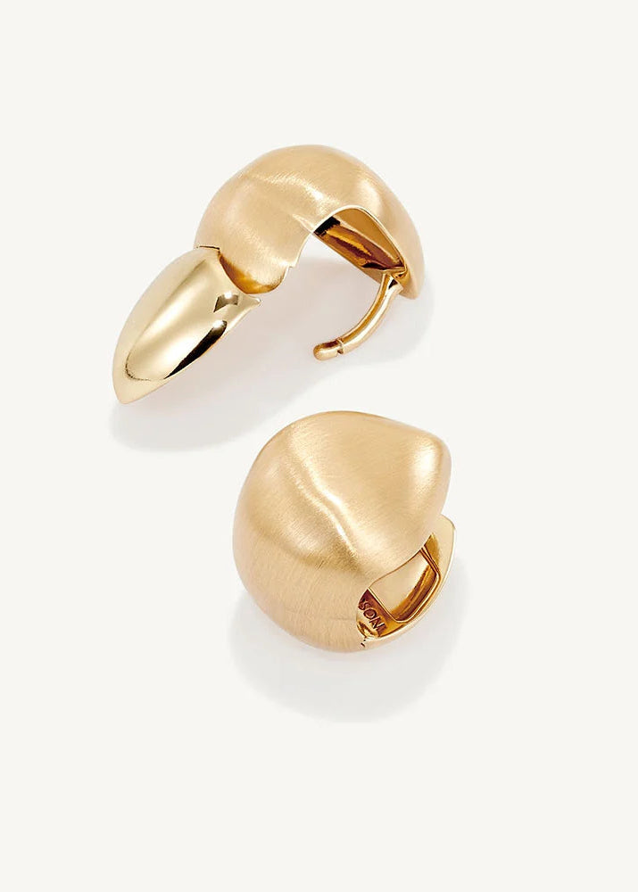 A pair of gold-toned, organic-shaped hoop earrings with a matte finish and a small polished hinge, displayed on a clean off-white background.