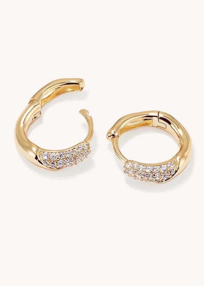 A pair of gold huggie hoop earrings with pavé-set clear stones on the front, displayed on a clean off-white background.