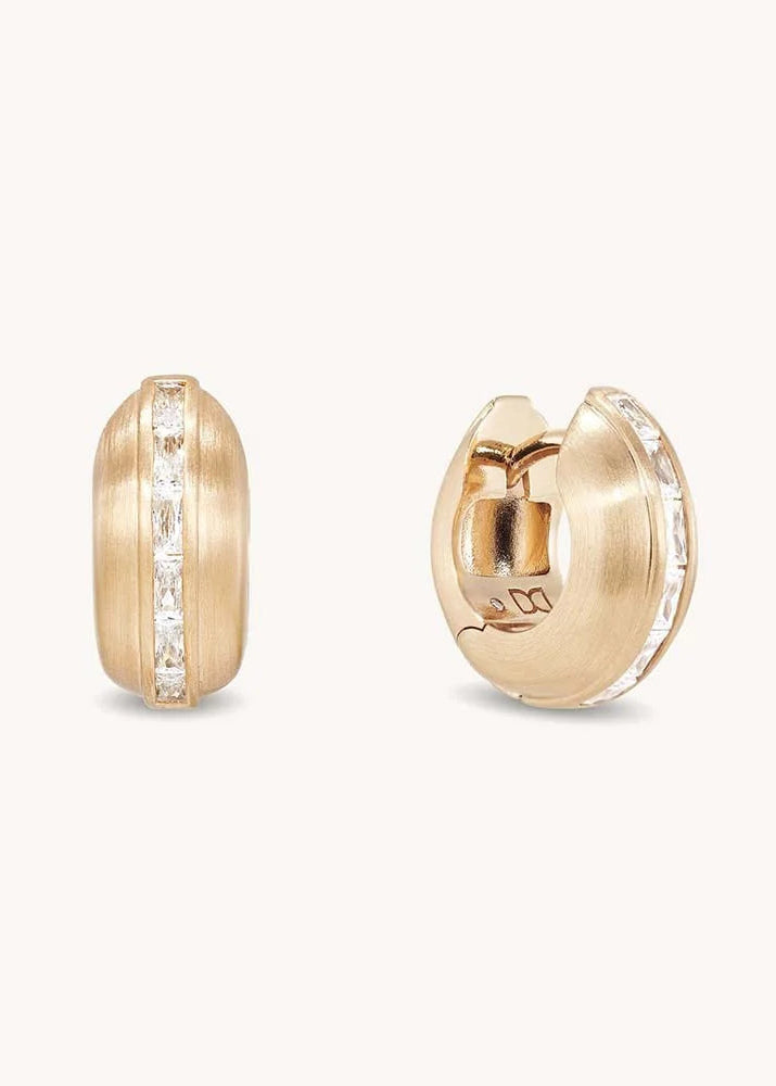 A pair of gold huggie hoop earrings with a channel-set row of clear baguette diamonds, shown from both front and side angles on a light cream background.