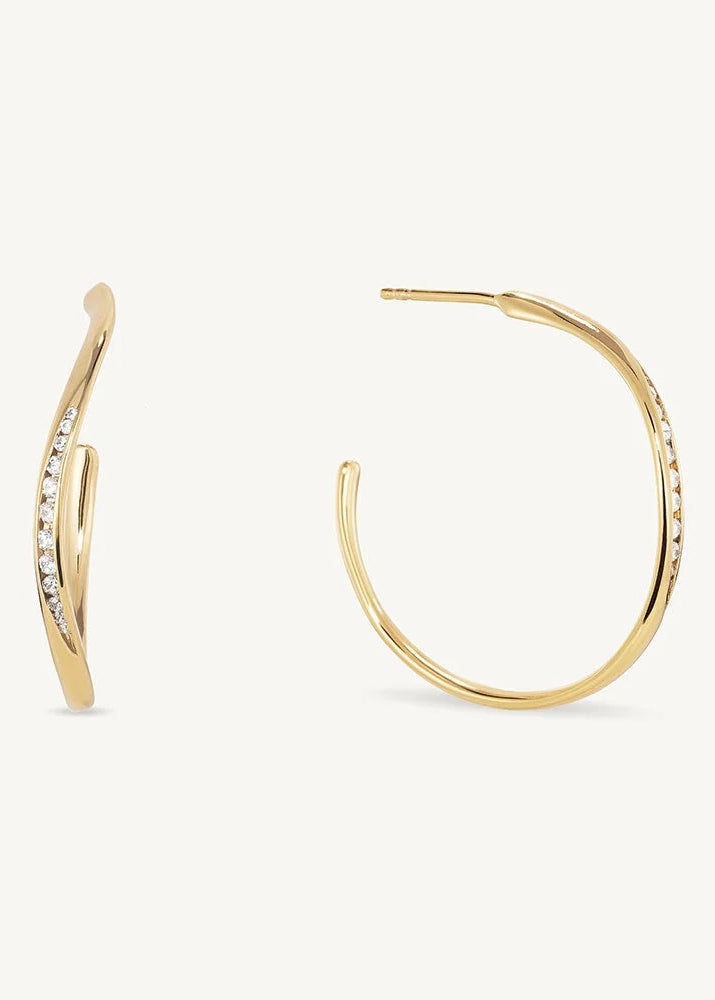 A pair of gold hoop earrings with small clear stones set along the front, shown on a clean off-white background.