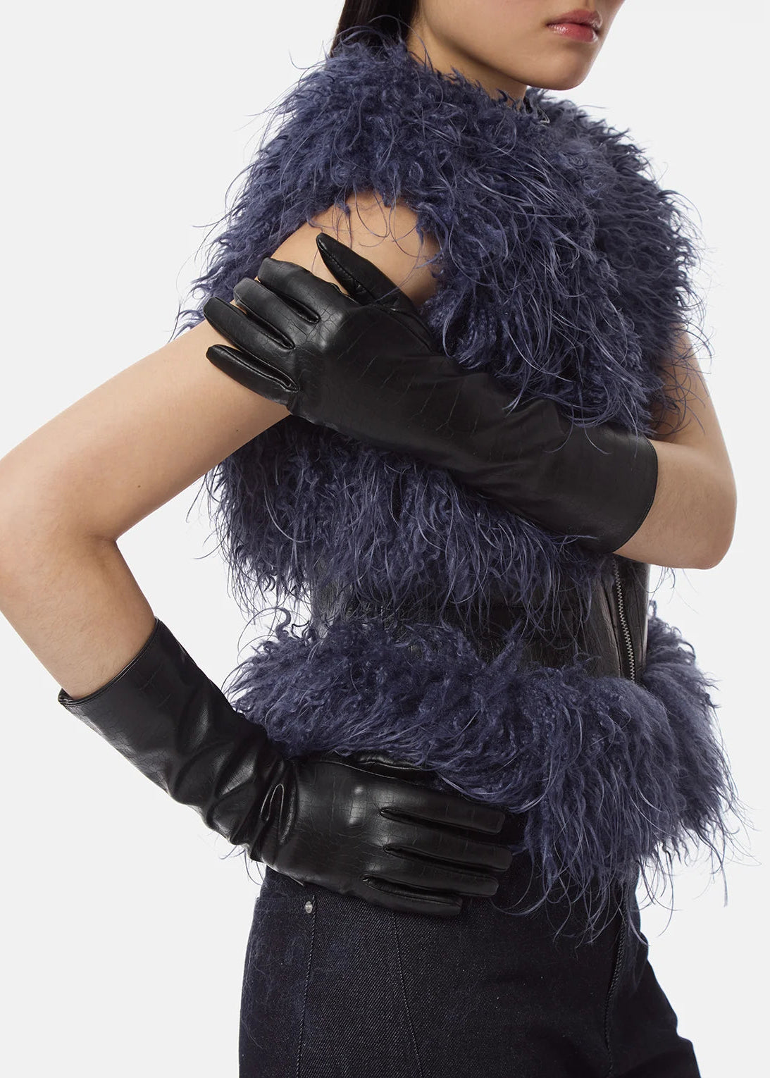 A model wearing a dark blue-purple feathered faux-fur vest with black leather gloves, shown from the chest down against a light gray background.