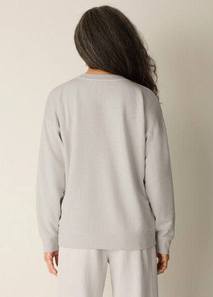 Person wearing a light gray sweatshirt and white pants against a plain background