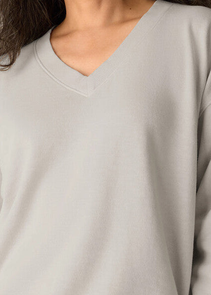 Close-up of a person wearing a light gray V-neck long-sleeve top, showing the neckline, chest area, and part of the hair.