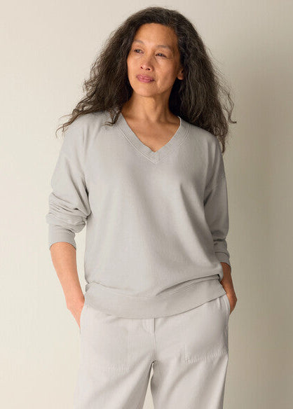 Woman wearing a light gray sweatshirt and white pants against a plain background
