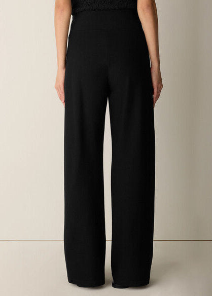 A model shown from the back wearing high-waisted, wide-leg black trousers against a plain beige studio background.