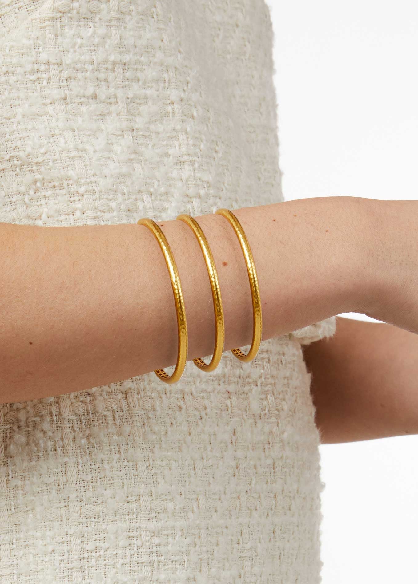 Gold bangles on a person's wrist with a neutral background