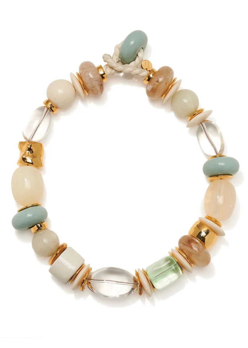 A beaded stretch bracelet featuring a mix of matte cream, sage green, light brown, and clear glass beads, accented with gold-toned spacers and a white rope clasp, shown on a white background.
