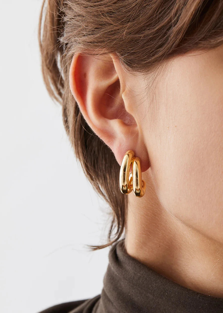 Gold hoop earrings worn by a person with a neutral background