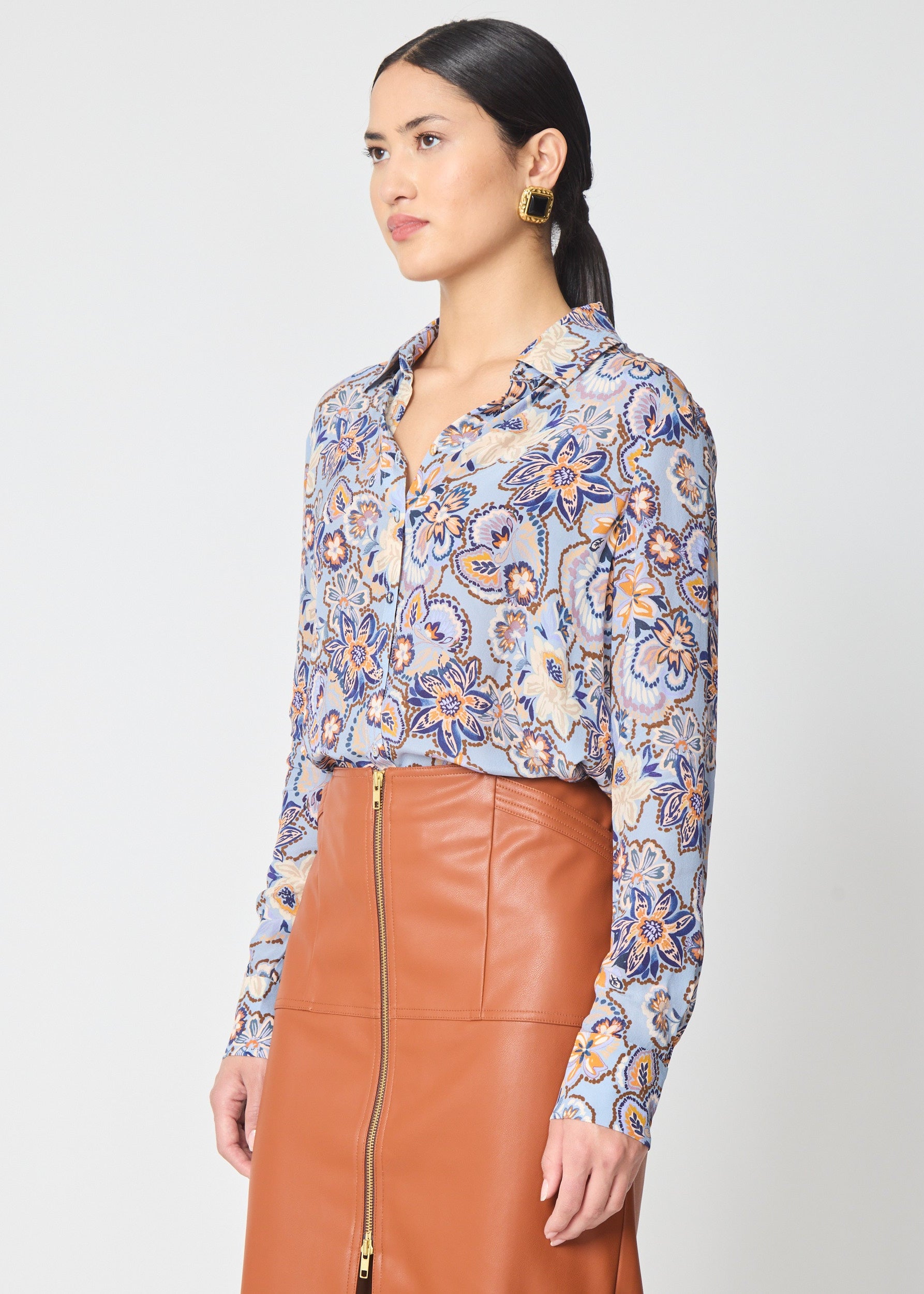 Woman wearing a patterned blouse and brown leather skirt on a white background