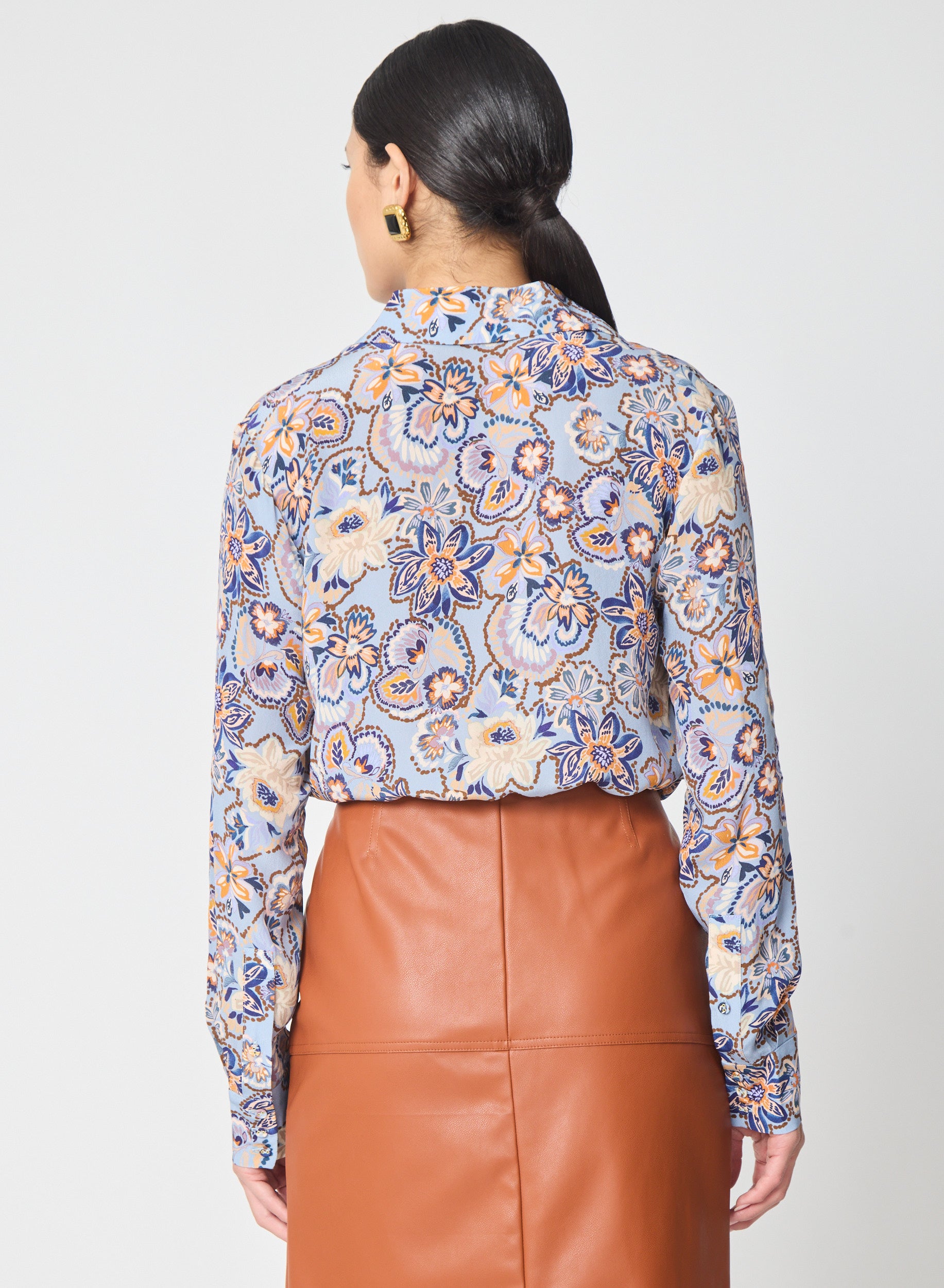 Woman wearing a patterned blouse and brown leather skirt on a white background