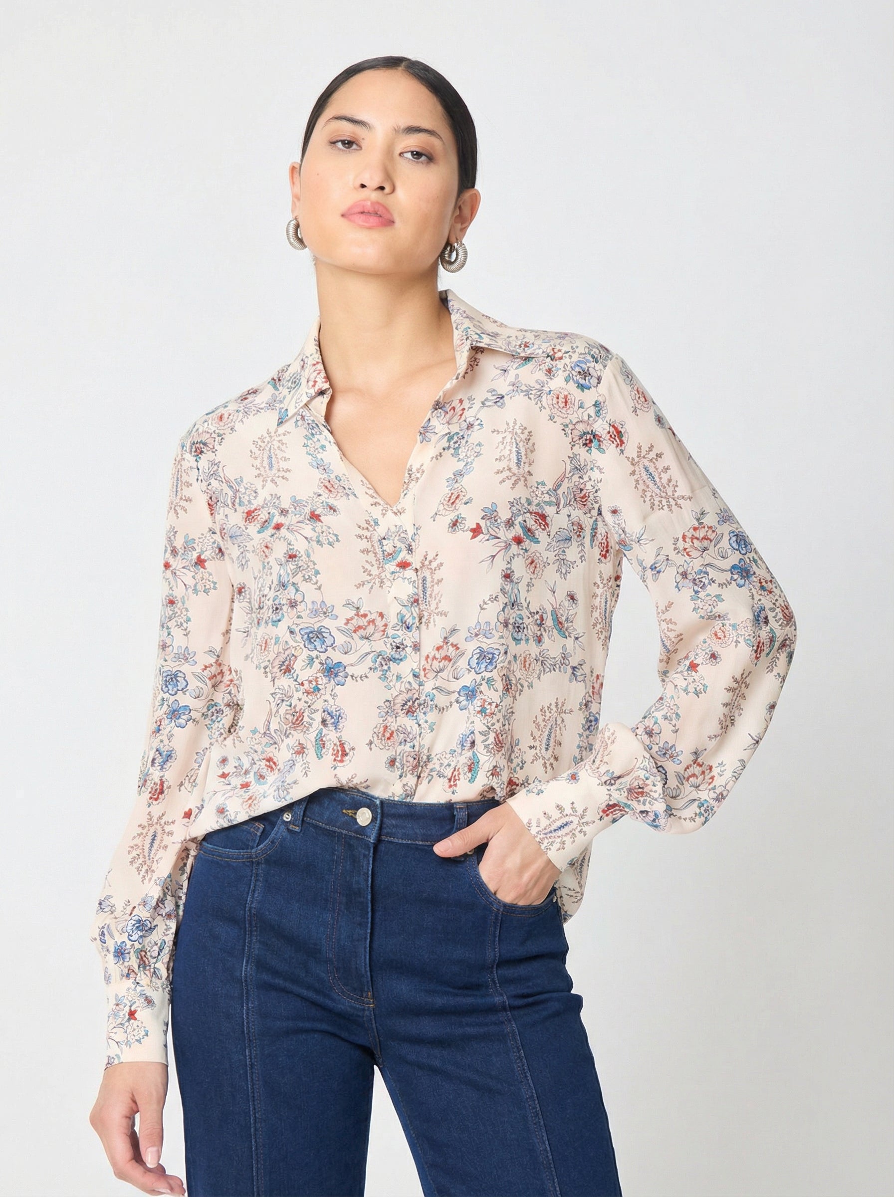 Woman wearing a floral blouse and blue jeans on a white background