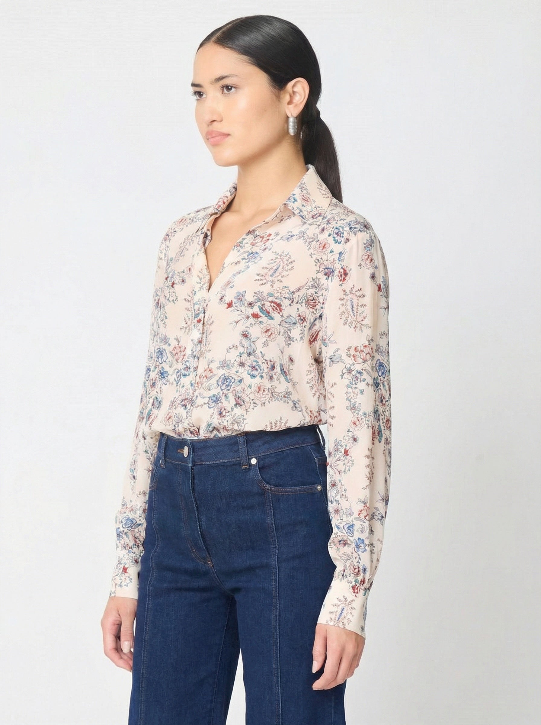 Woman wearing a floral blouse and blue jeans against a white background