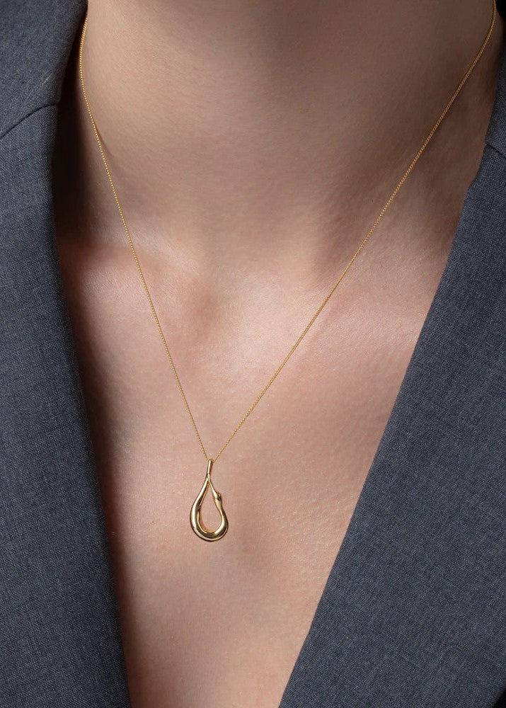 Gold necklace with a teardrop pendant on a person wearing a dark blazer.