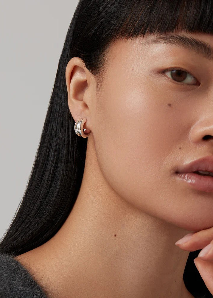 Close-up of a person wearing silver earrings with a neutral background