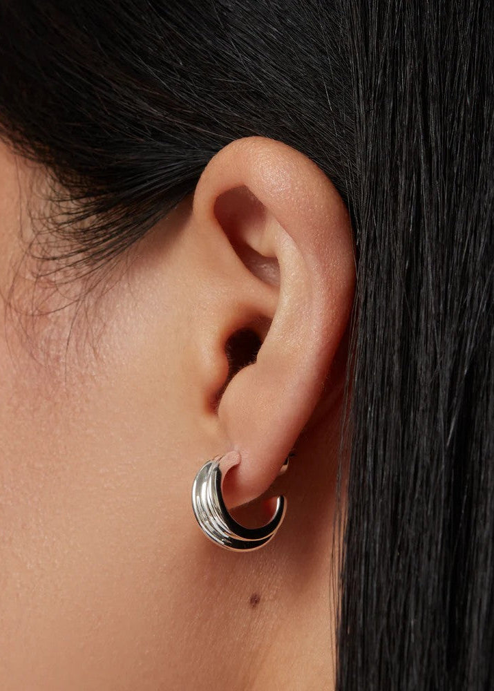 Close-up of an ear wearing a silver hoop earring with dark hair in the background