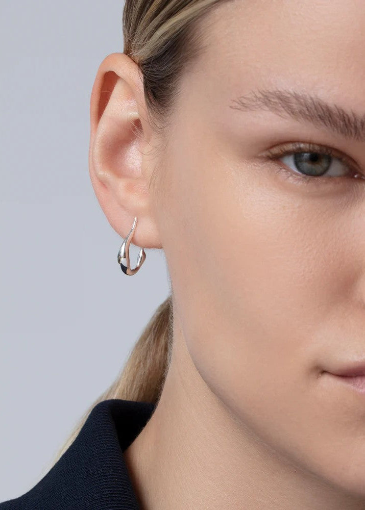 Close-up of a person wearing a silver hoop earring against a neutral background