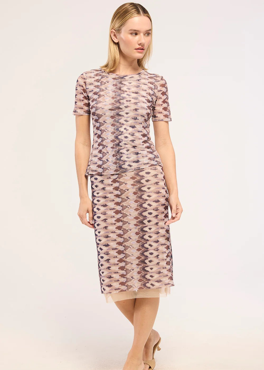 A woman modeling a short-sleeve midi dress with a beige, brown, and pink geometric pattern, photographed against a plain light background.
