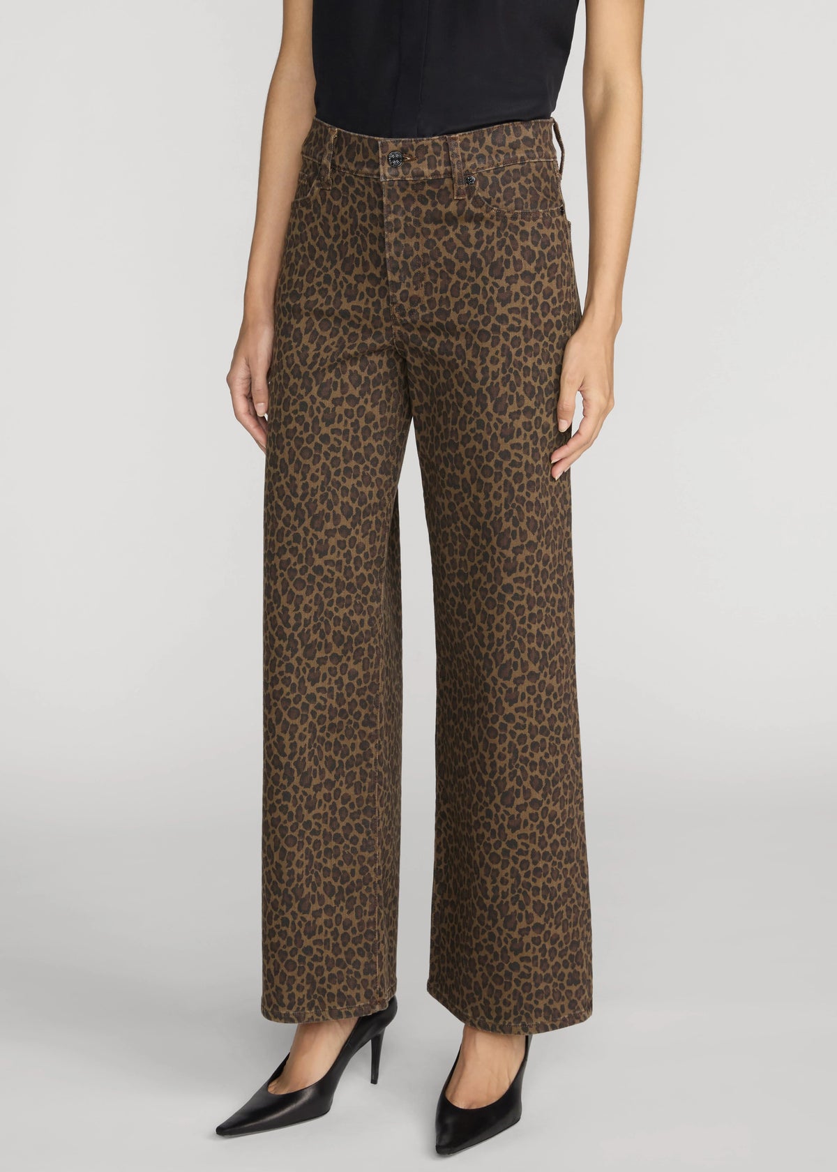 A model wearing brown leopard-print wide-leg pants with a black top and black pointed-toe heels, shown from the waist down on a light gray studio background.