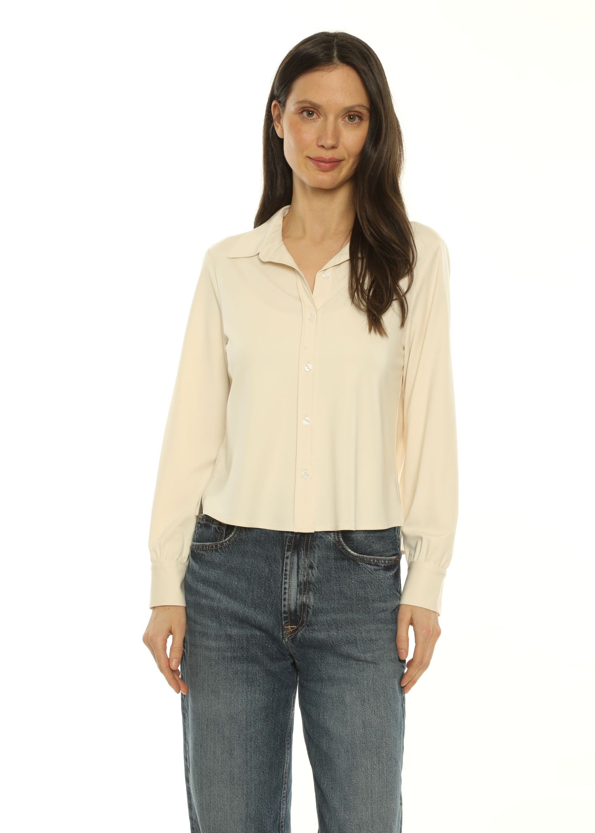 A woman wearing a cream-colored long-sleeve button-up shirt and dark blue jeans, shown from a side profile against a plain white background.
