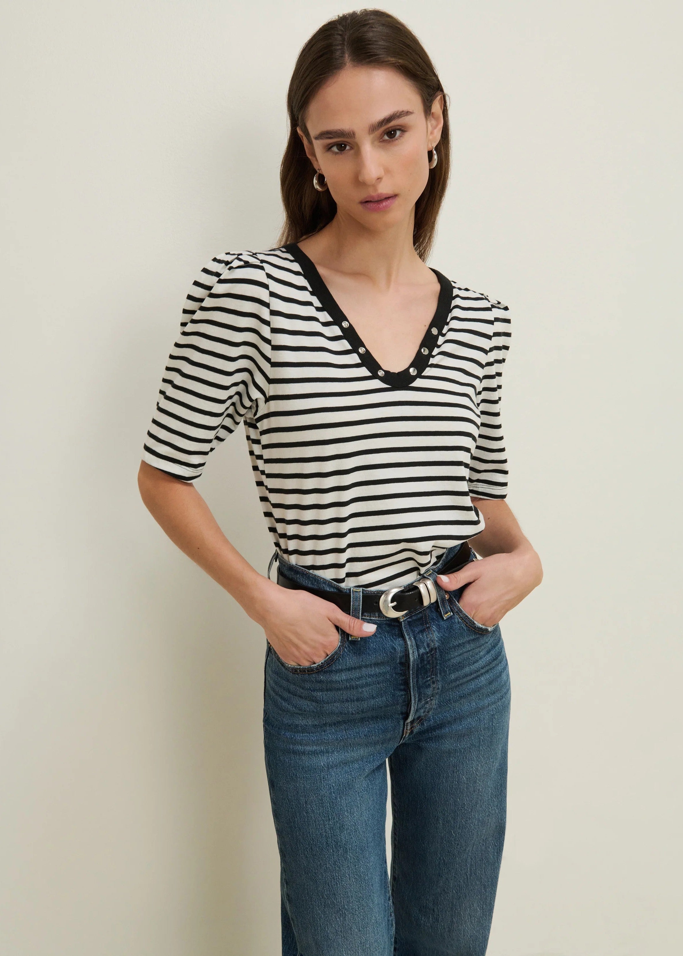 Woman wearing a black and white striped shirt with blue jeans against a plain background