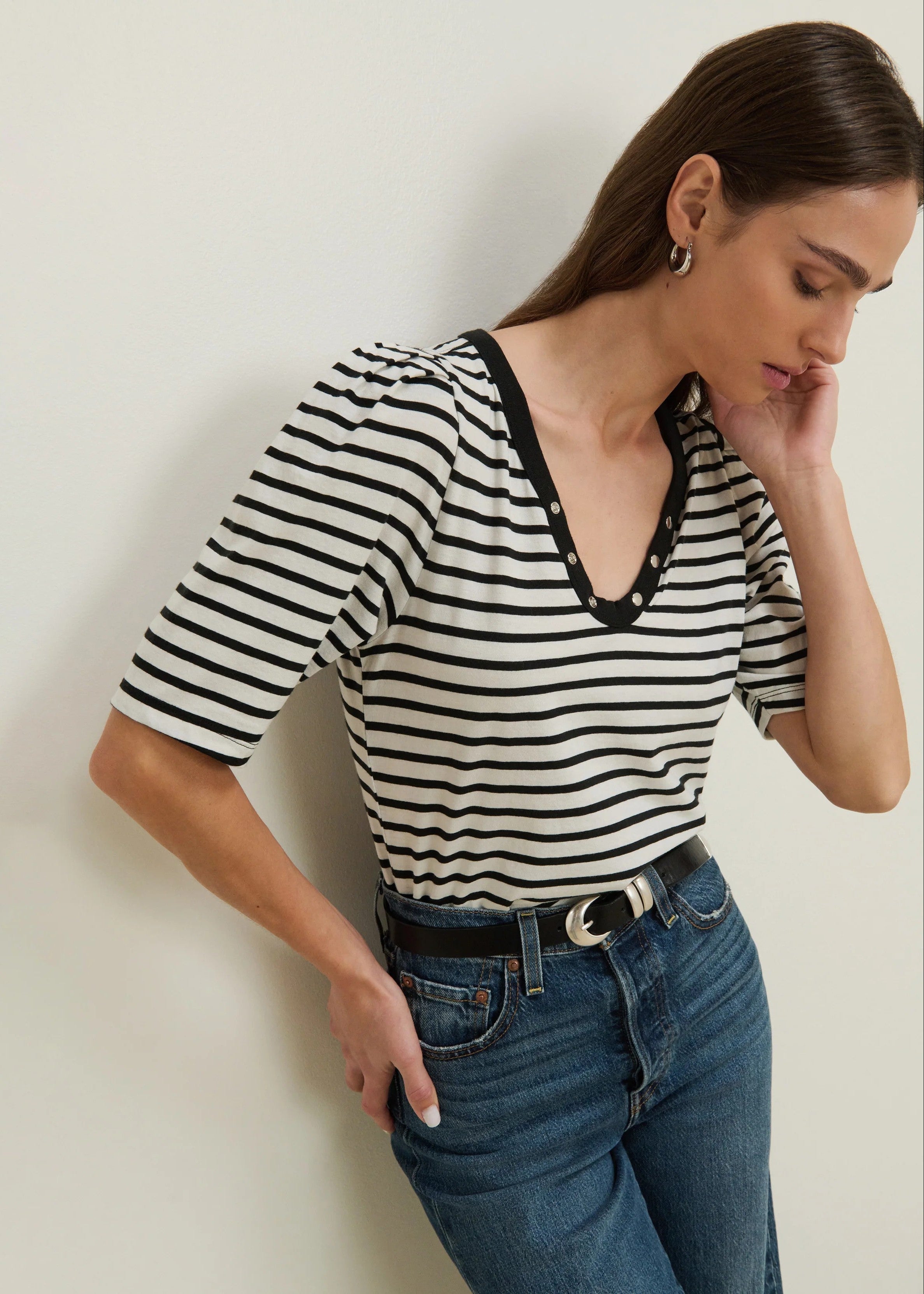 Woman wearing a black and white striped shirt and blue jeans against a plain background