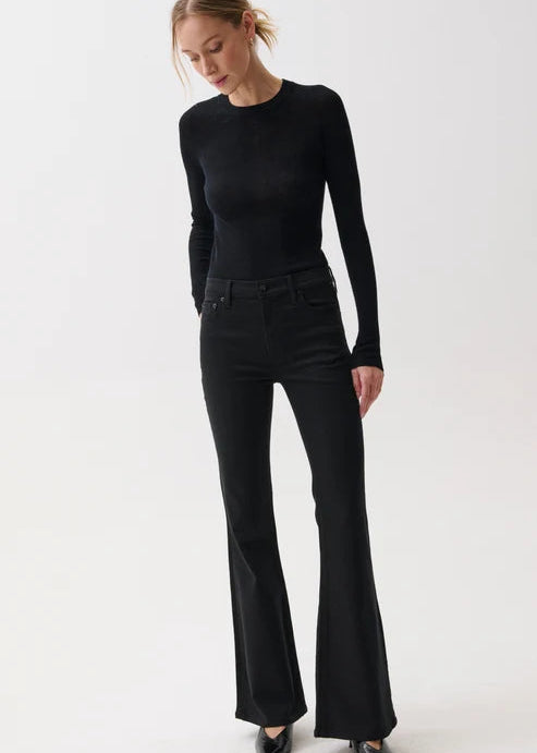 A woman modeling a black long-sleeve crewneck top and black flared jeans against a plain light gray studio background.