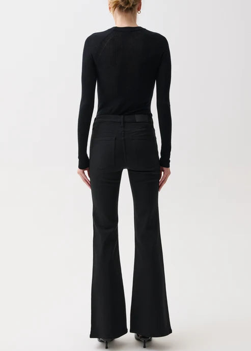 A woman viewed from the back wearing a black long-sleeve top and black flared pants against a plain light gray studio background.