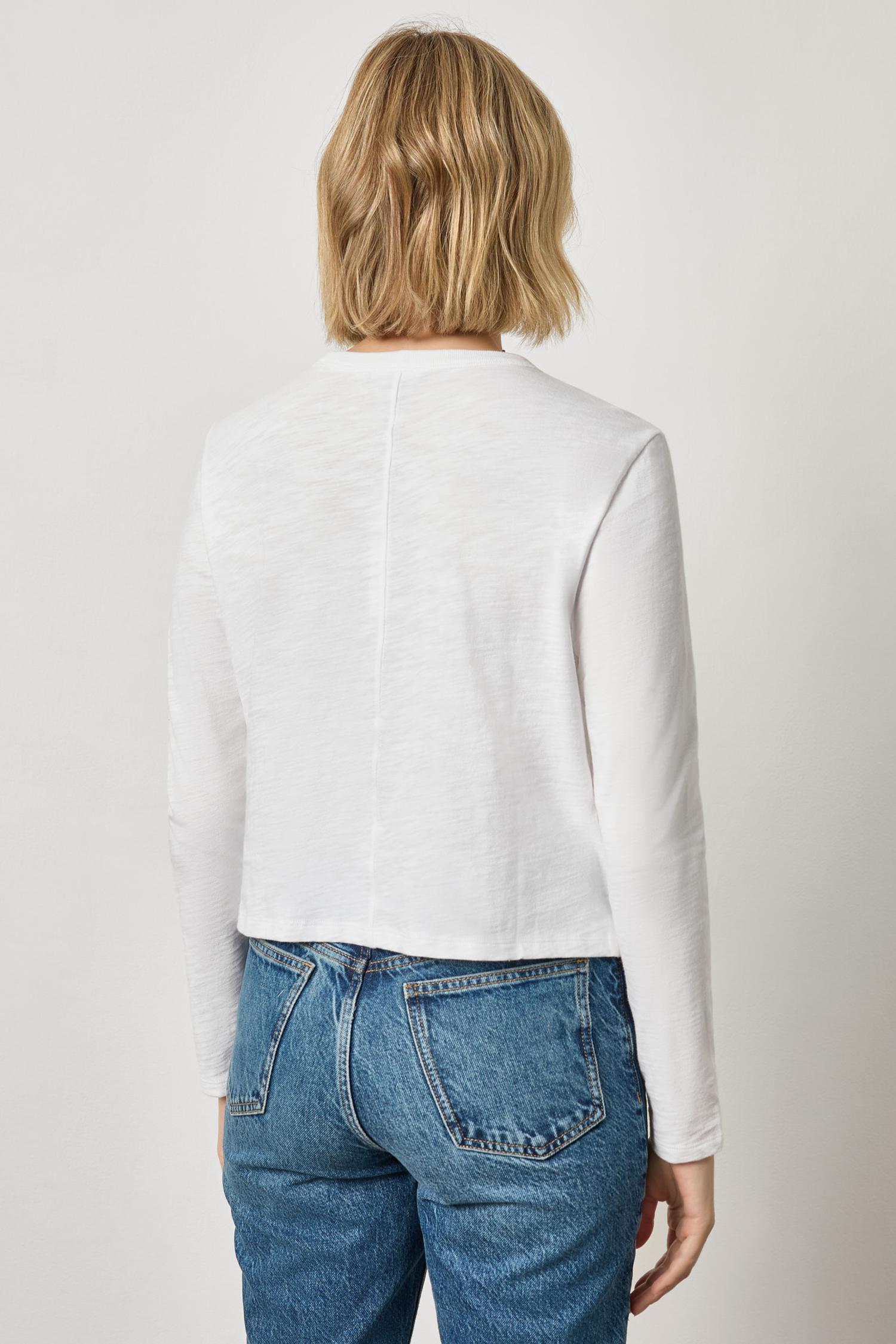 Person wearing a white long-sleeve shirt and blue jeans on a plain background