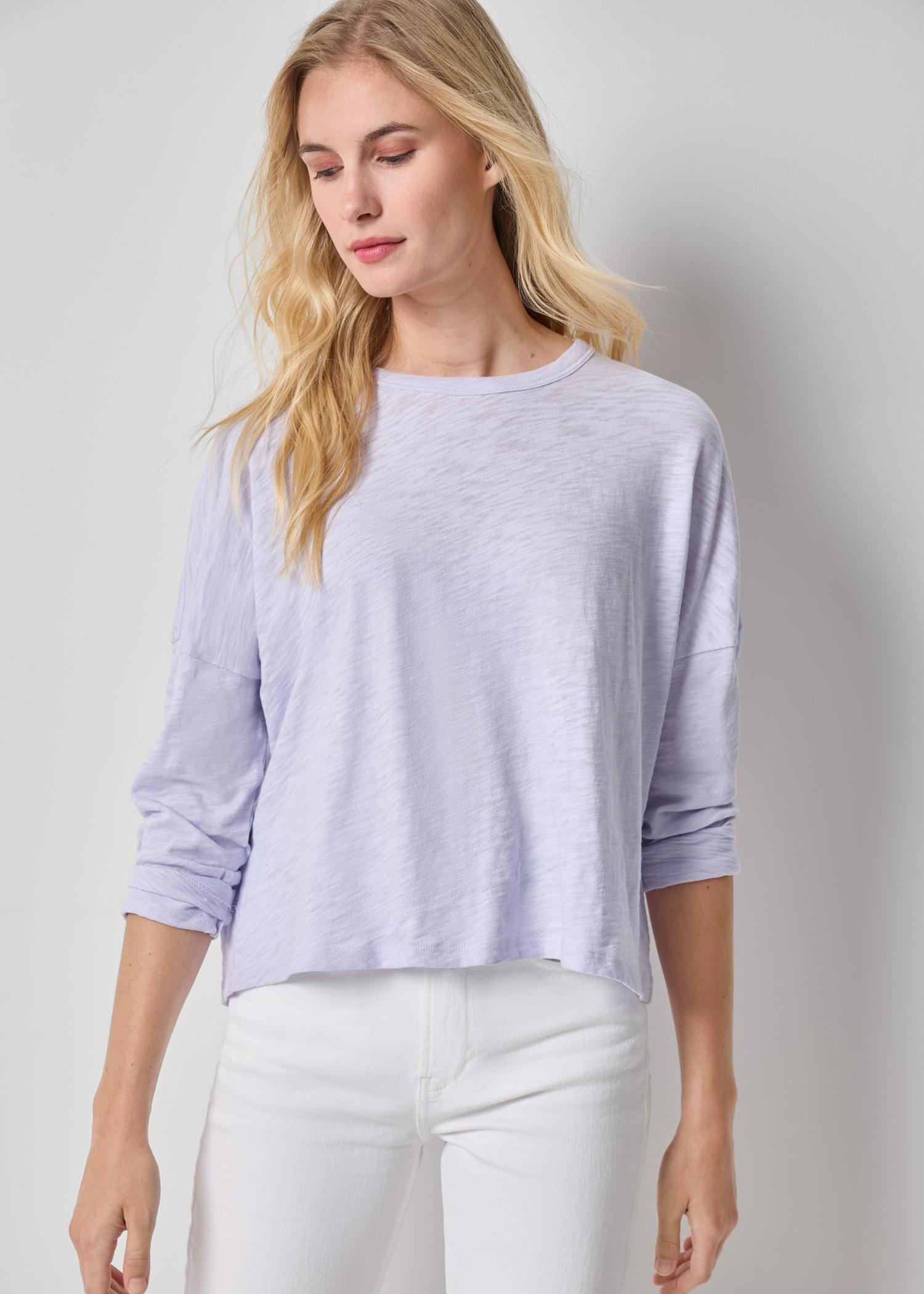 Woman wearing a light purple sweater and white pants on a white background