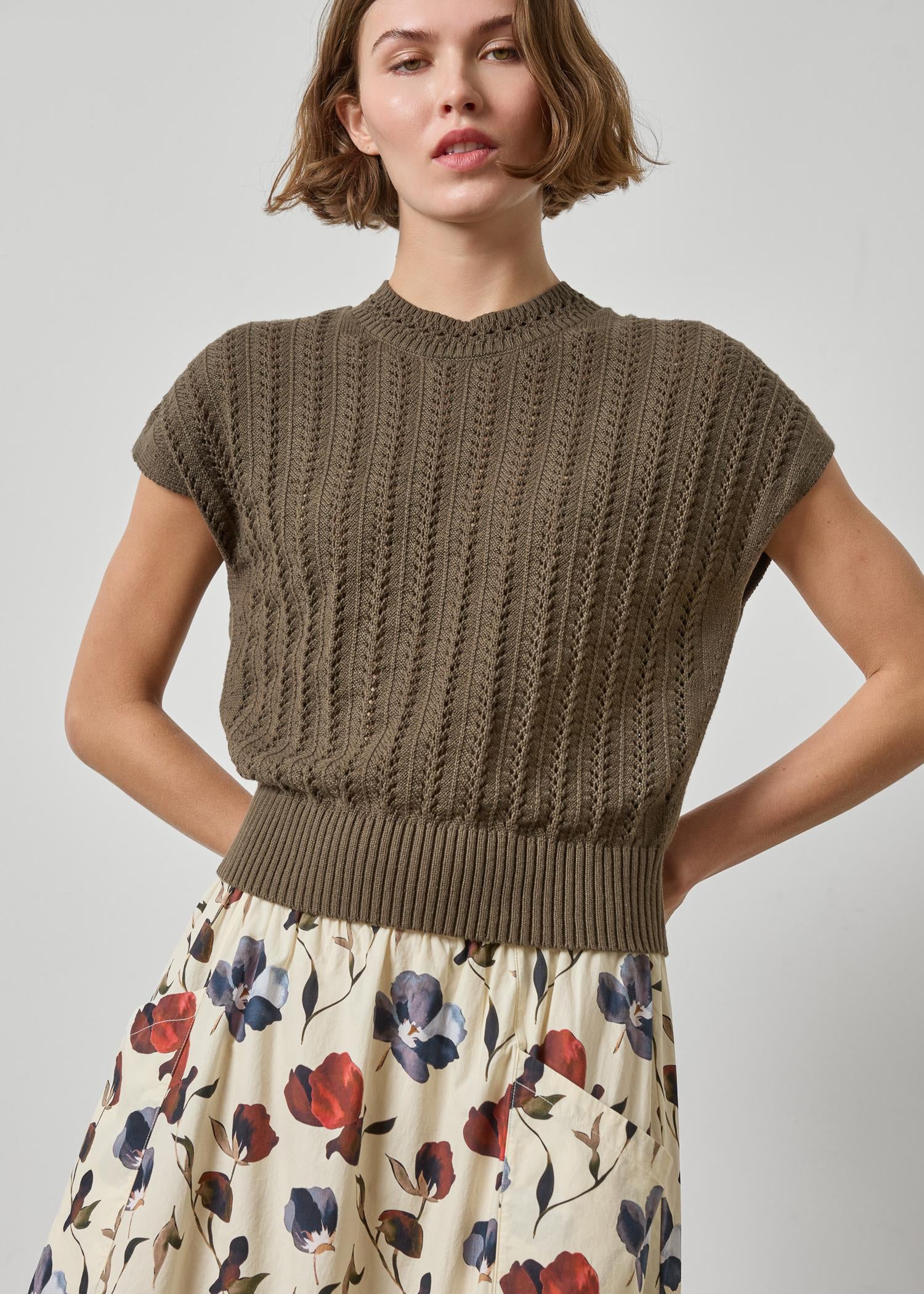 Woman wearing a brown knitted top and floral skirt on a plain background
