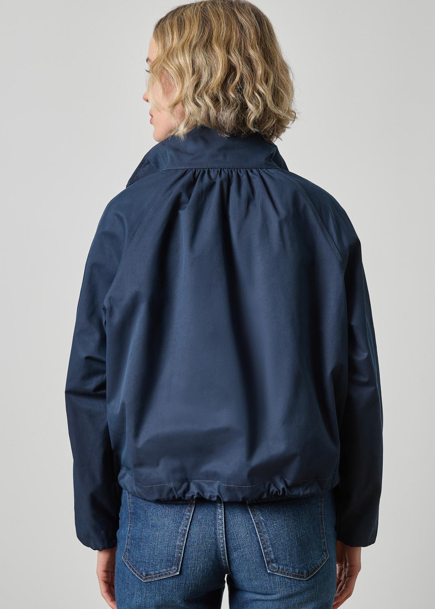Person wearing a navy blue jacket and jeans on a plain background