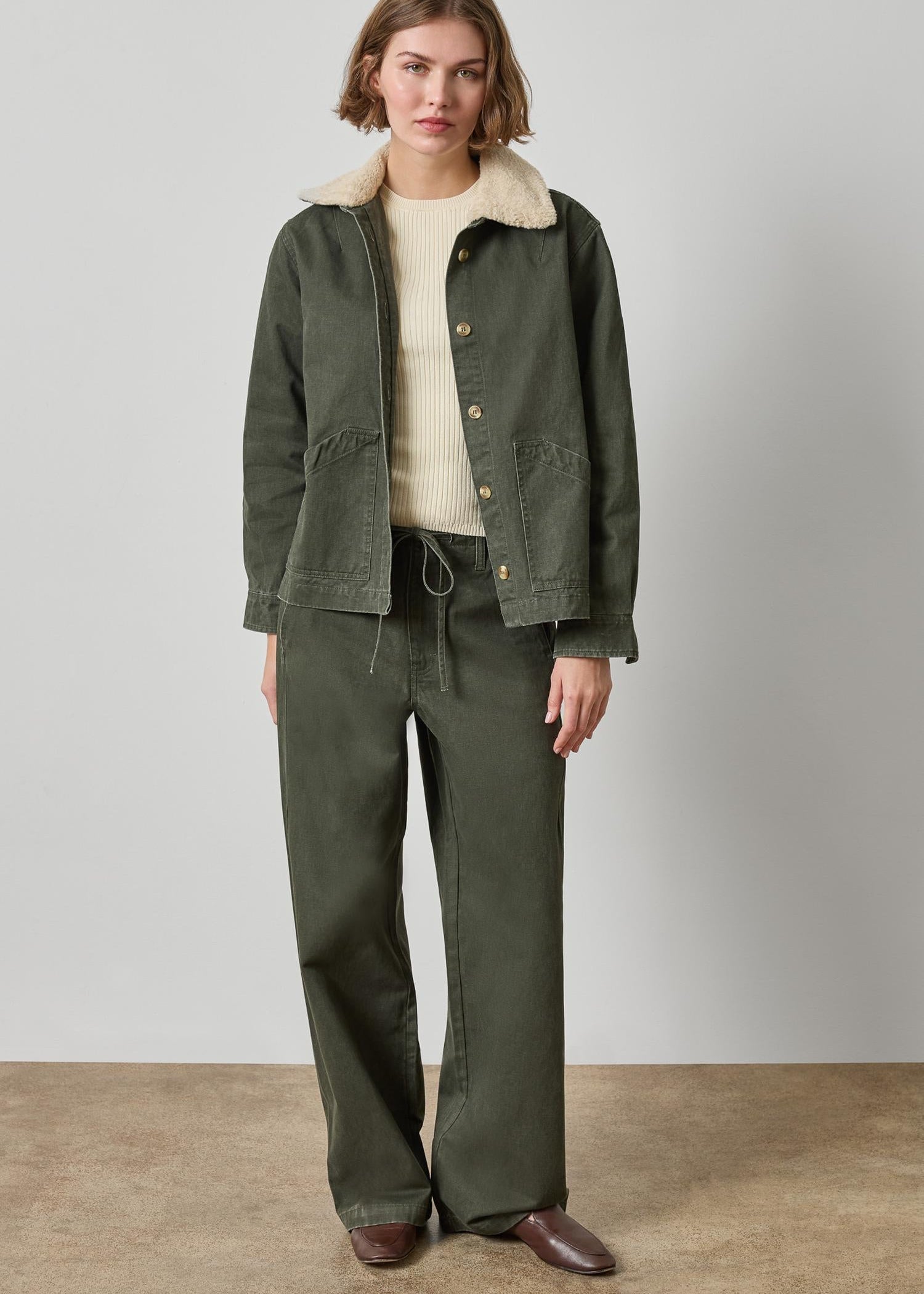 Woman wearing a green jacket and pants with a beige shirt against a plain background